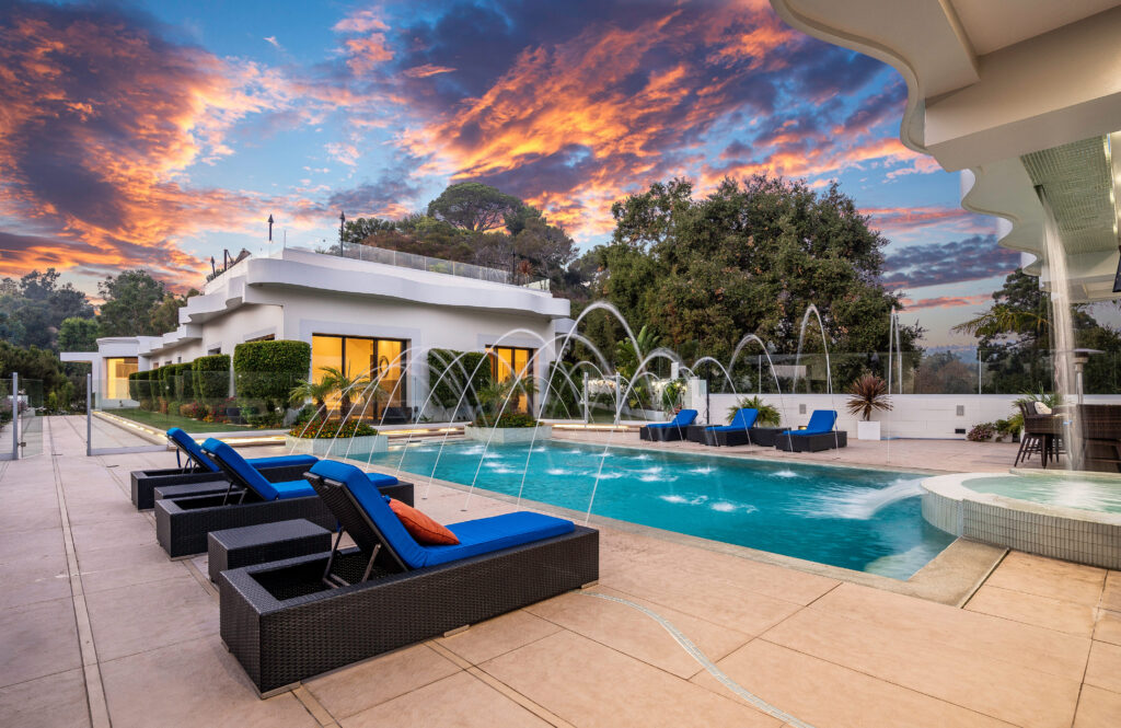Stunning sunset over a modern pool area featuring lounge chairs, water fountains, and lush greenery around a luxurious home | swimming pool makers qatar